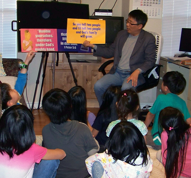 A CEF Houston teacher shows a Bible lesson visual to a group of children sitting on the floor.